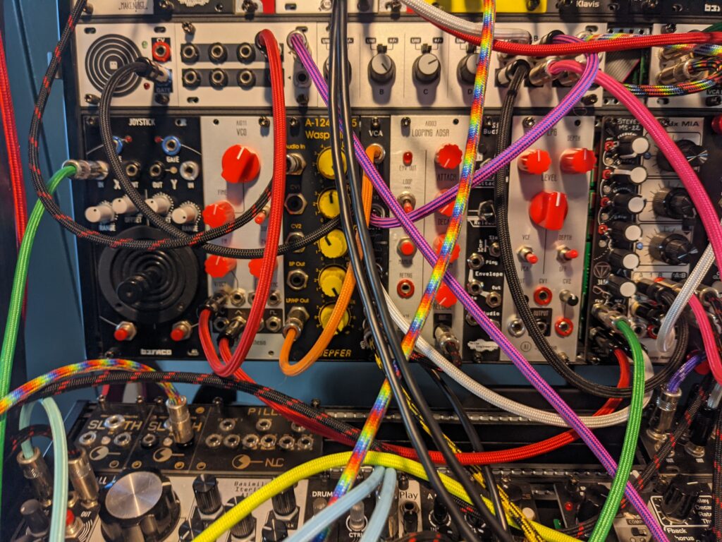 closeup image of Bbartokk's modular synthesizer with colourful cables plugged into it. there are many colourful knobs and lights